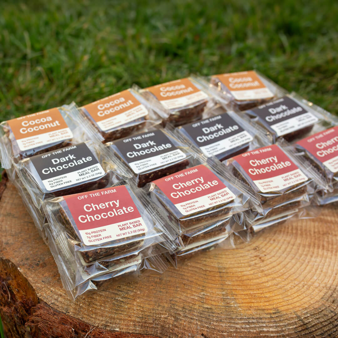 Assorted meal bars in clear packaging on a wooden surface with grass in the background