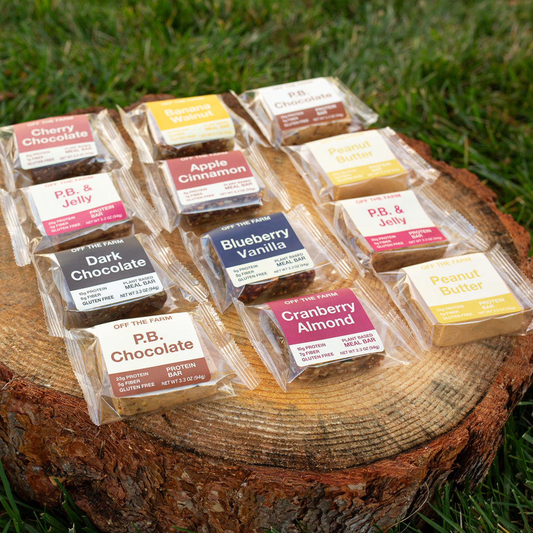 Assorted protein and meal bars in clear packaging on a wooden log outdoors.