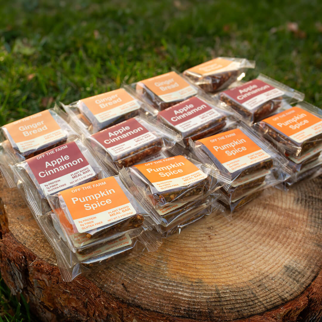 Assorted pumpkin spice and apple cinnamon flavored meal bars on a wooden log outdoors.