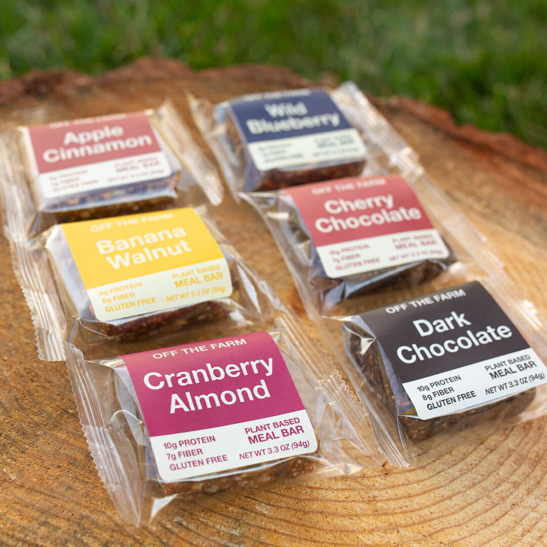 Assorted plant-based meal bars on a wooden surface with grass in the background