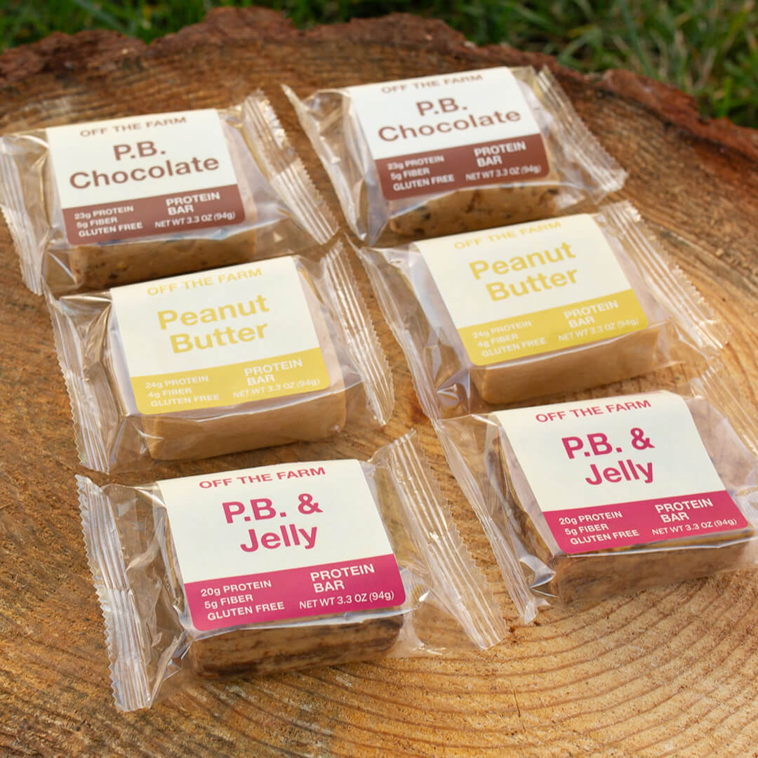 Packaged protein bars labeled 'P.B. Chocolate', 'Peanut Butter', and 'P.B. & Jelly' on a wooden surface.