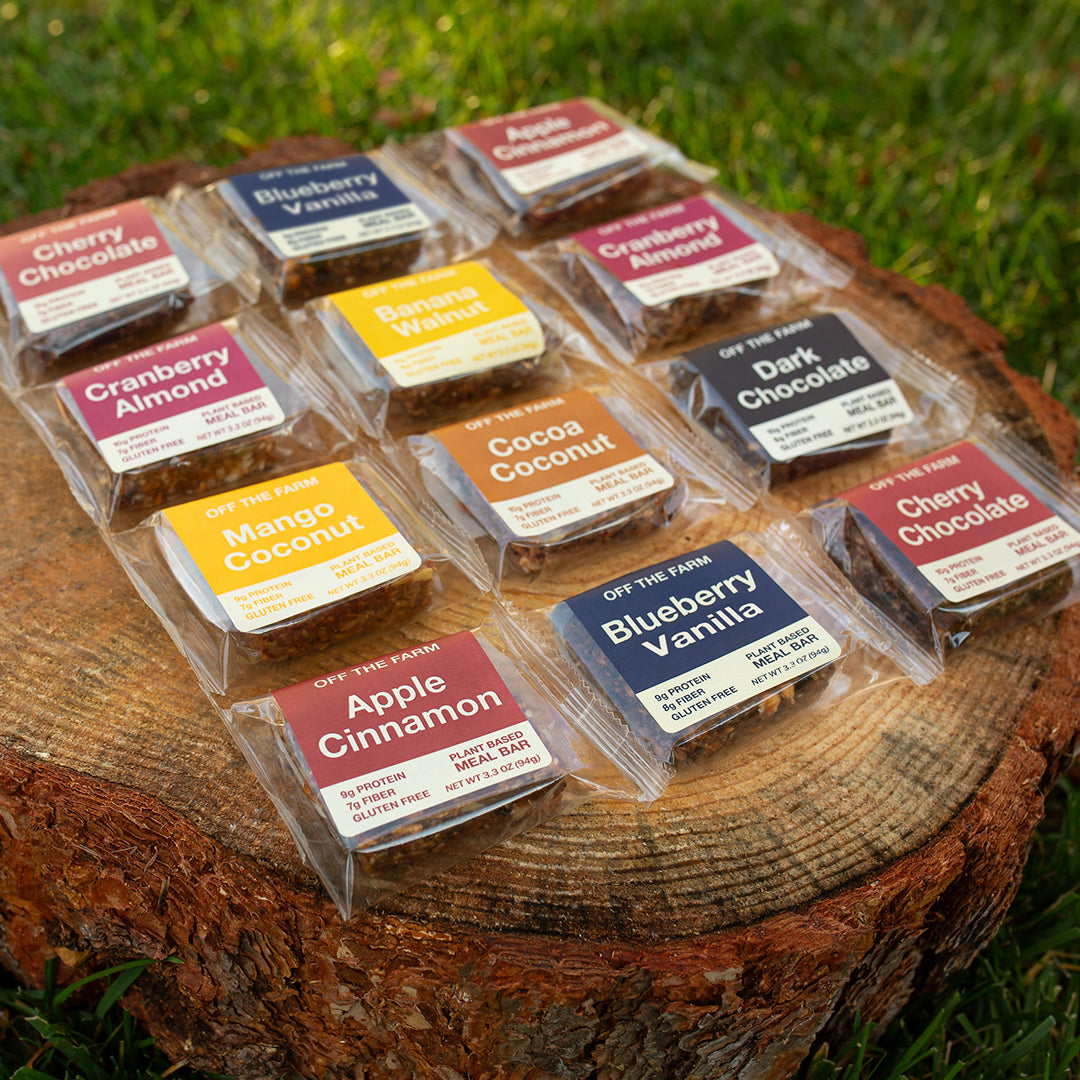 Assorted meal bars in clear packaging on a wooden log outdoors.