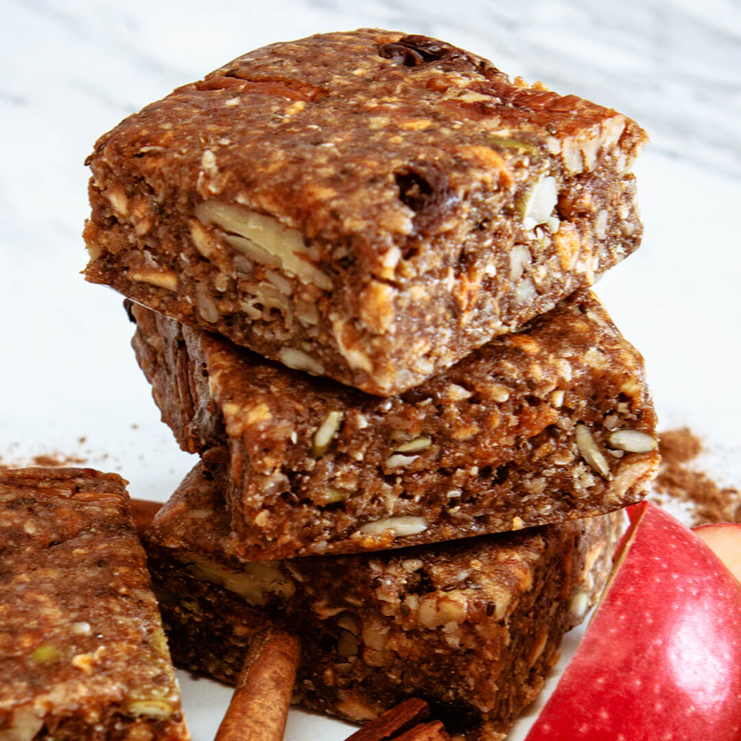 Stack of granola bars with an apple and cinnamon stick on a white background