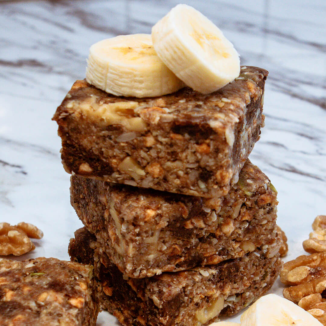 Stack of banana walnut bars with banana slices on a marble surface