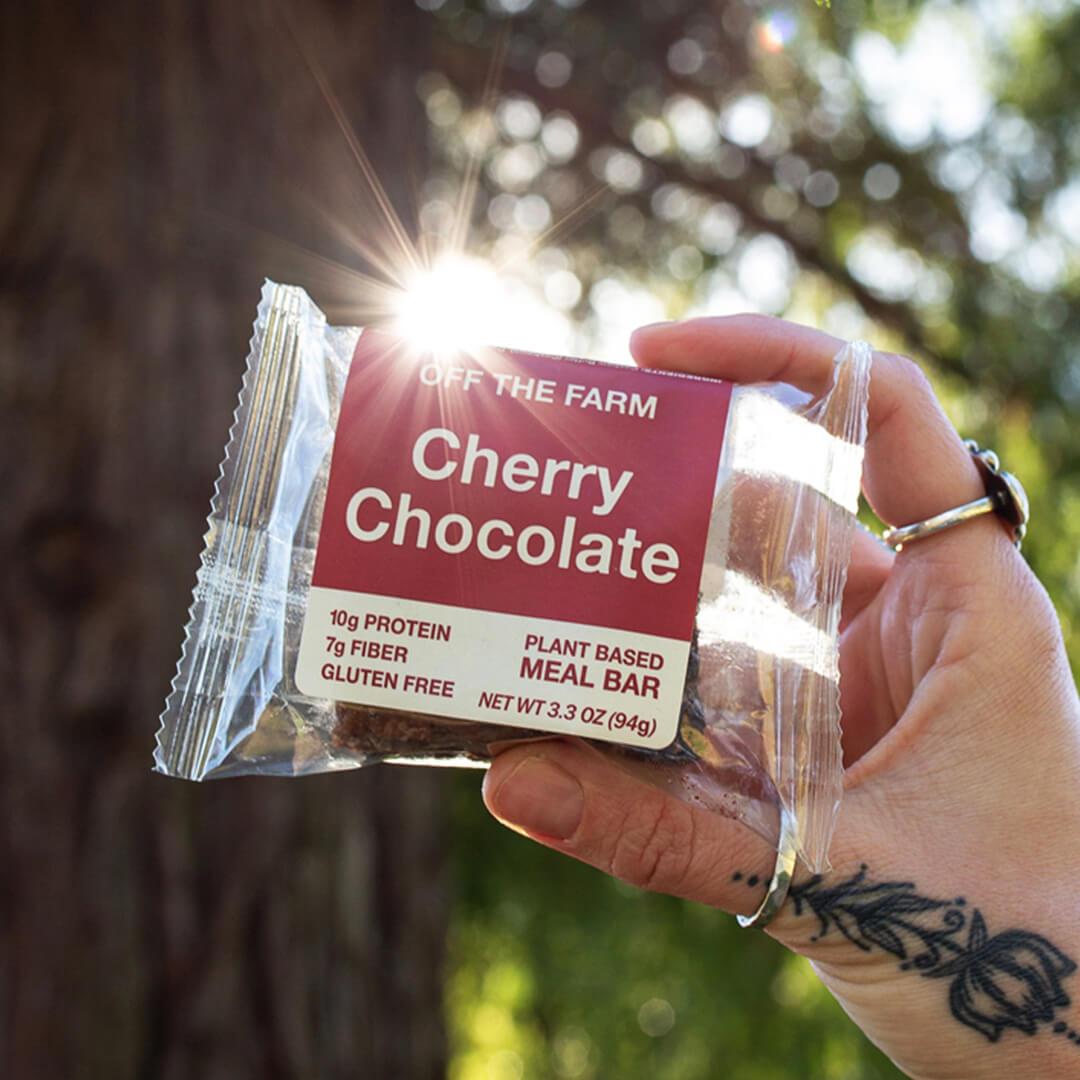 Hand holding a 'Cherry Chocolate' meal bar package with a natural background
