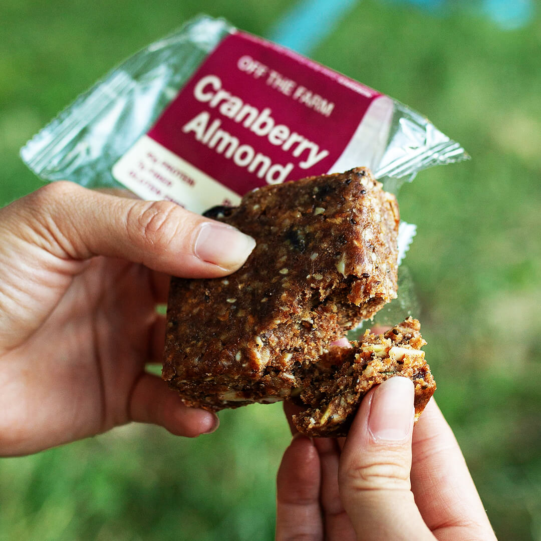 Hand holding a cranberry almond meal bar with packaging in the background