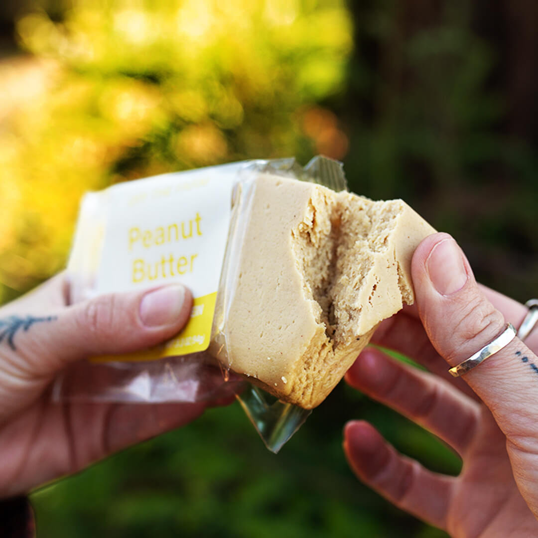 Person holding a piece of peanut butter protein bar with a blurred green background