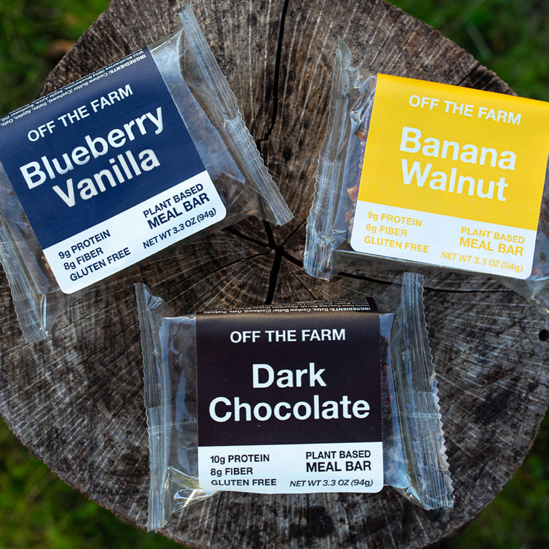 Three plant-based meal bars from 'Off The Farm' on a wooden surface.