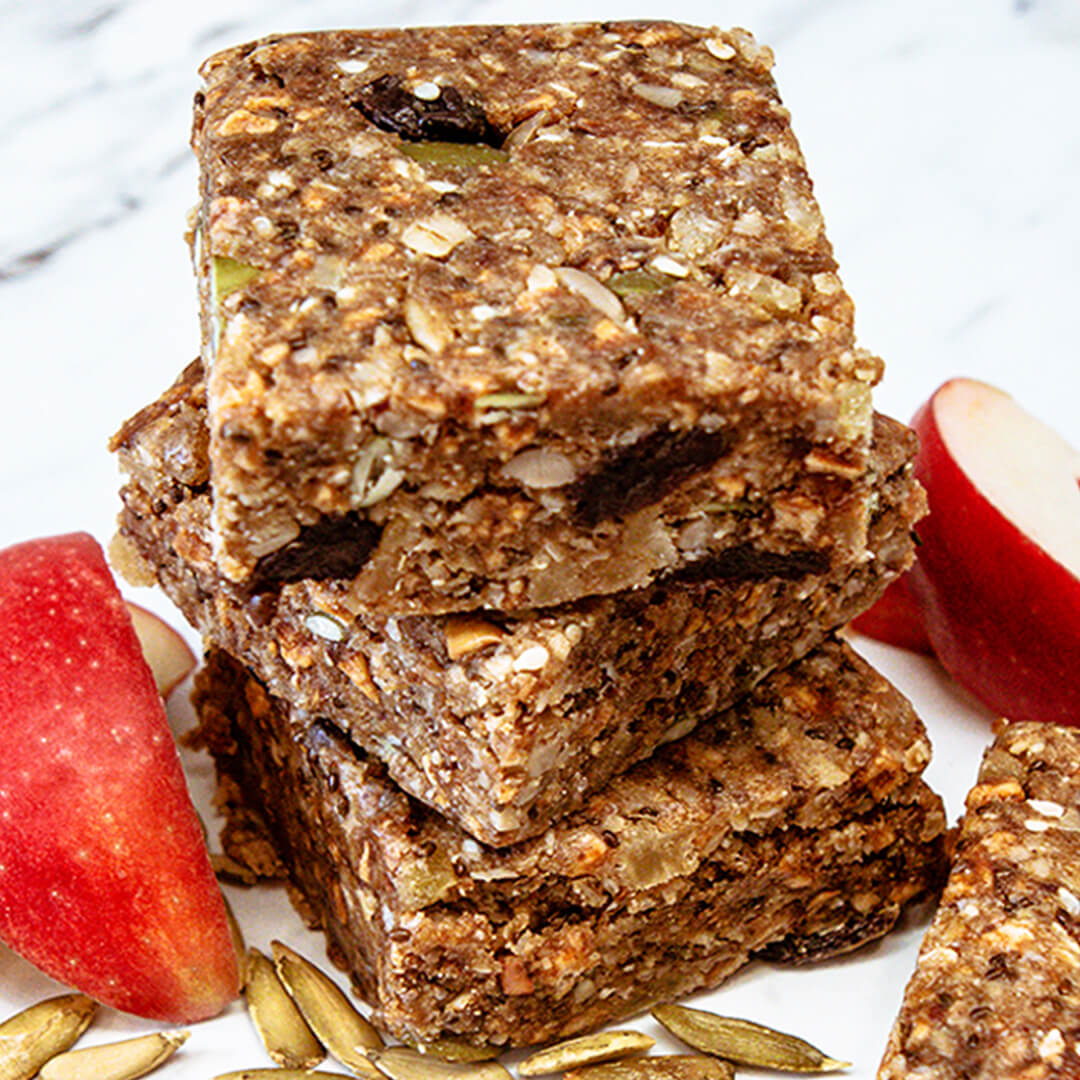 Stack of Off The Farm gingerbread bars with apples and seeds on a white plate