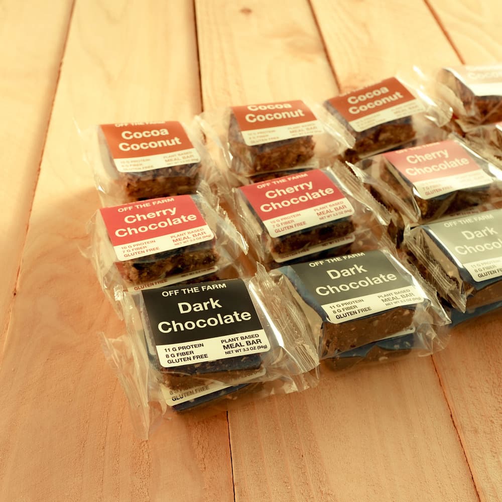 A collection of chocolate bars with different flavors including Cocoa Coconut, Cherry Chocolate, and Dark Chocolate, displayed on a wooden surface.