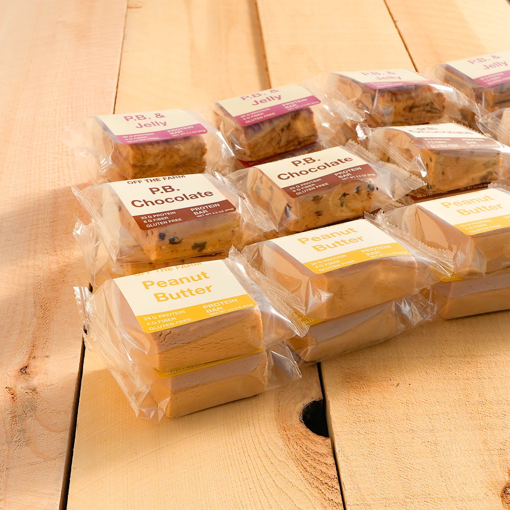 A variety of Off The Farm protein bars wrapped in clear packaging, labeled Peanut Butter, Peanut Butter Chocolate, and Peanut Butter & Jelly.