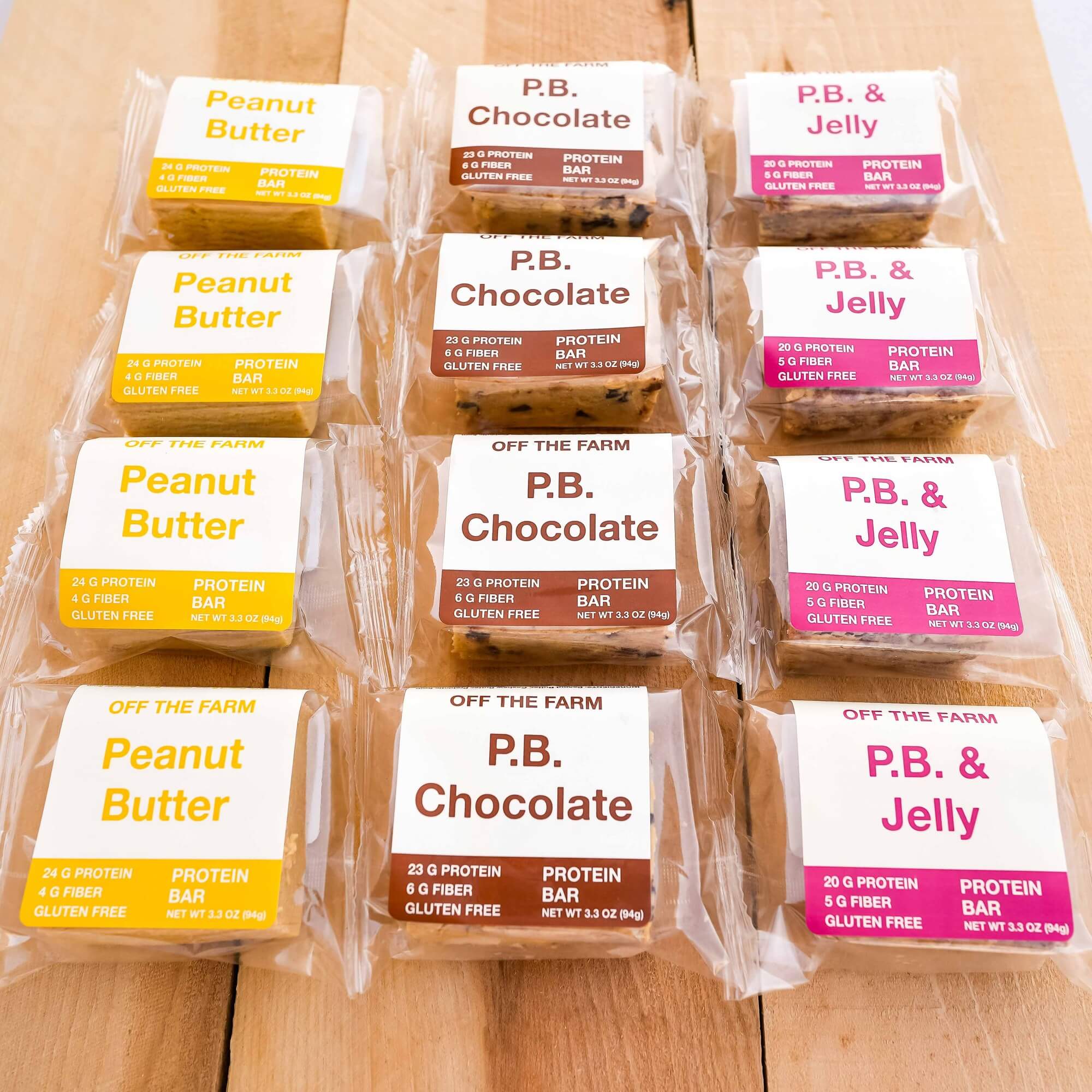 A selection of Off The Farm protein bars laid out on a wooden surface, with labels indicating different flavors such as Peanut Butter, Peanut Butter Chocolate, and Peanut Butter & Jelly.