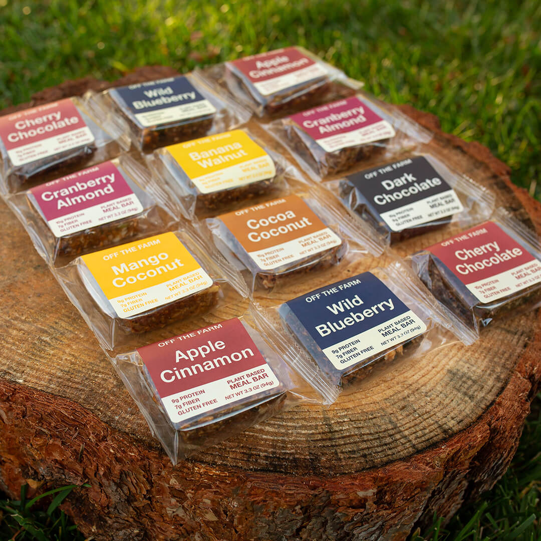 Assorted meal bars in clear packaging on a wooden log outdoors