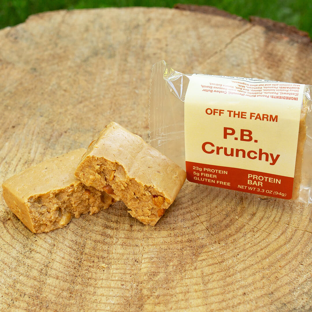 OFF THE FARM P.B. Crunchy protein bar split in half on a wooden surface 