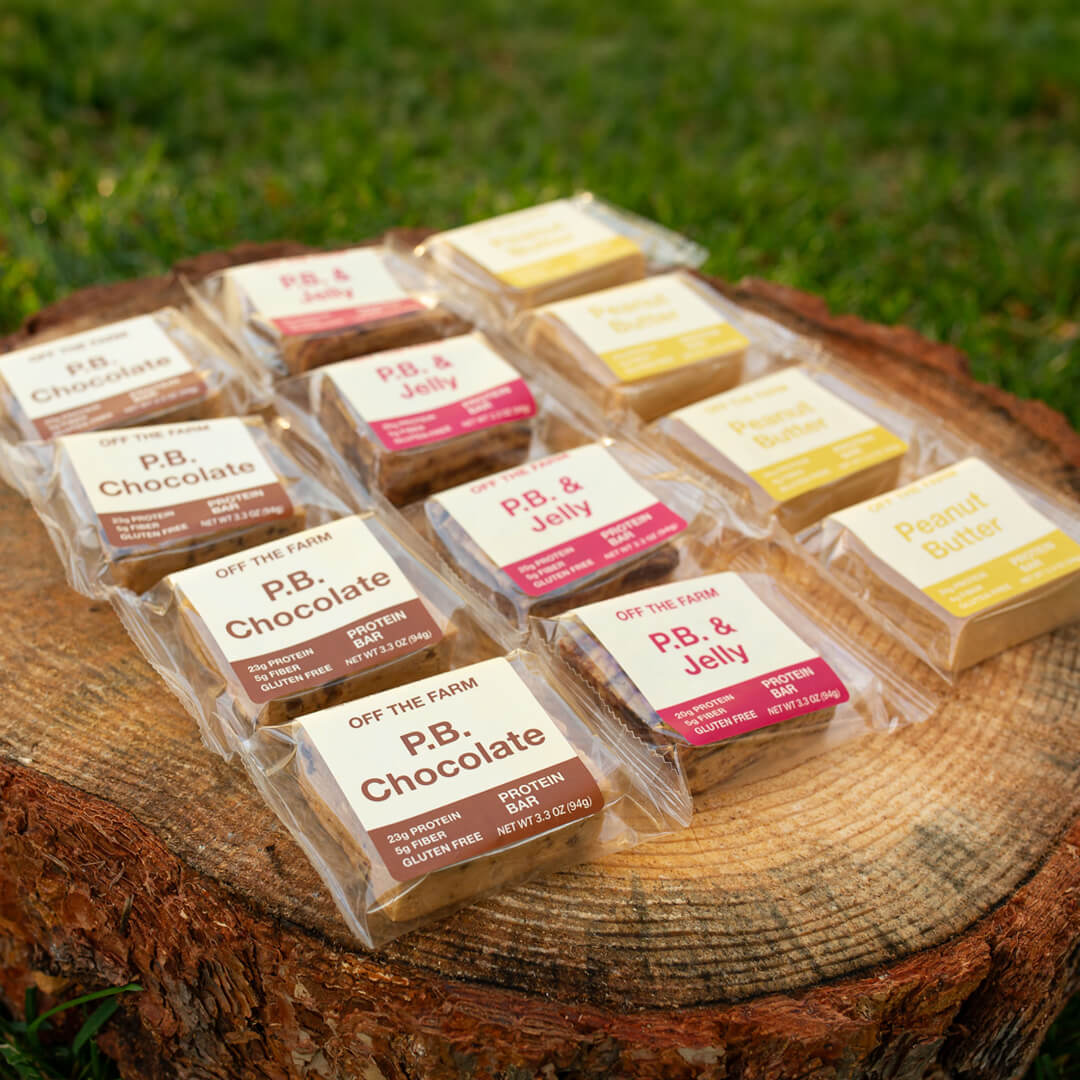 Assorted protein bars in clear packaging on a wooden log outdoors.