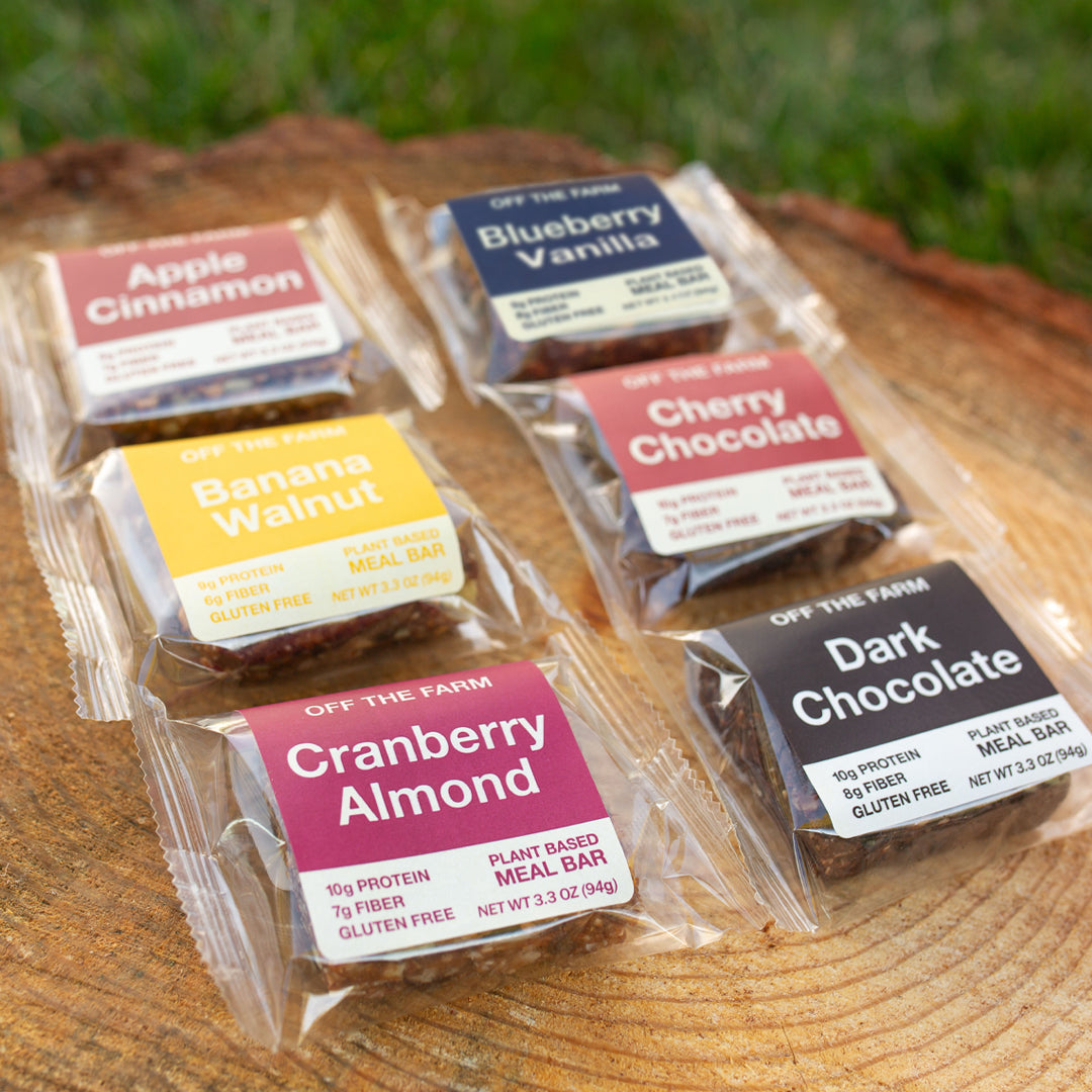 Assorted plant-based meal bars on a wooden surface with grass in the background