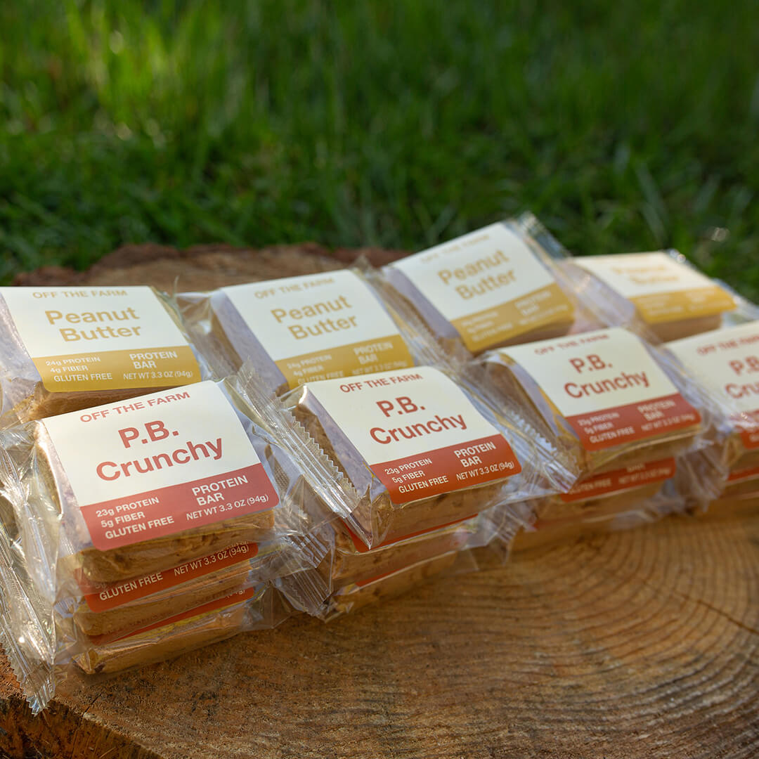 Several packaged protein bars arranged on a wooden surface outdoors, with green grass blurred in the background.