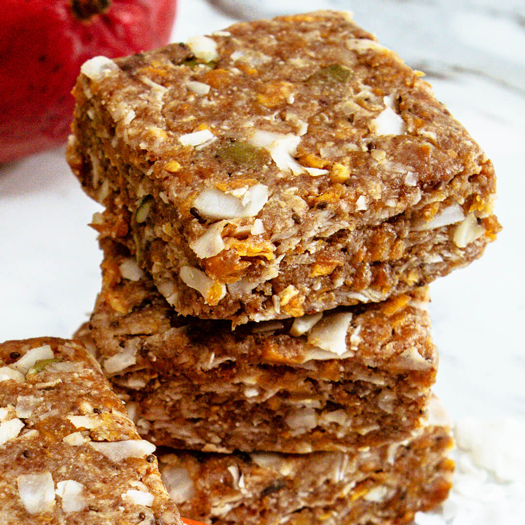 Stack of mango coconut meal bars with a blurred apple in the background