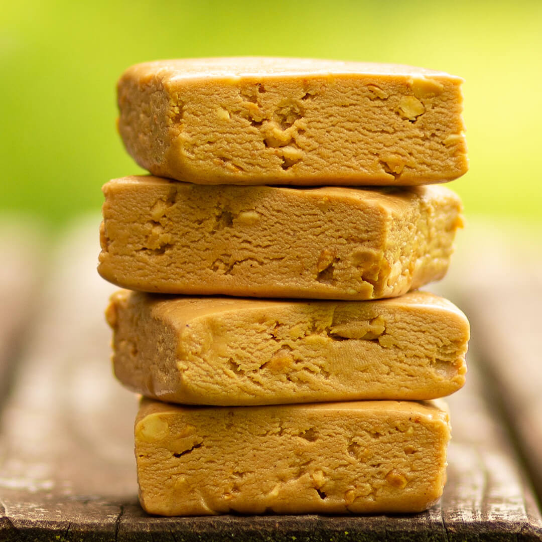 Stack of four peanut butter crunchy bars on a wooden surface with a blurred green background