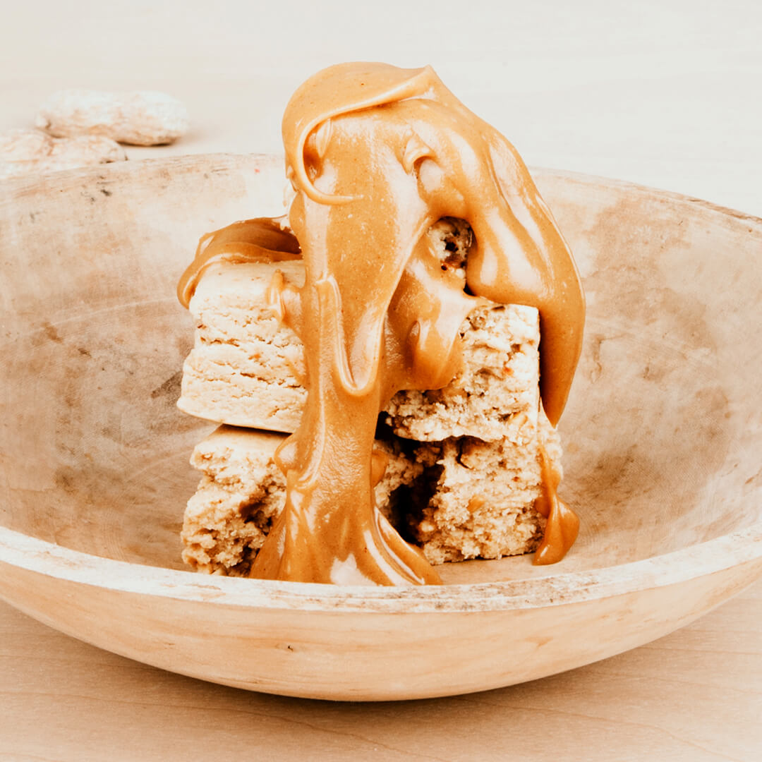 Wooden bowl with two peanut butter protein bars and peanut butter on top.