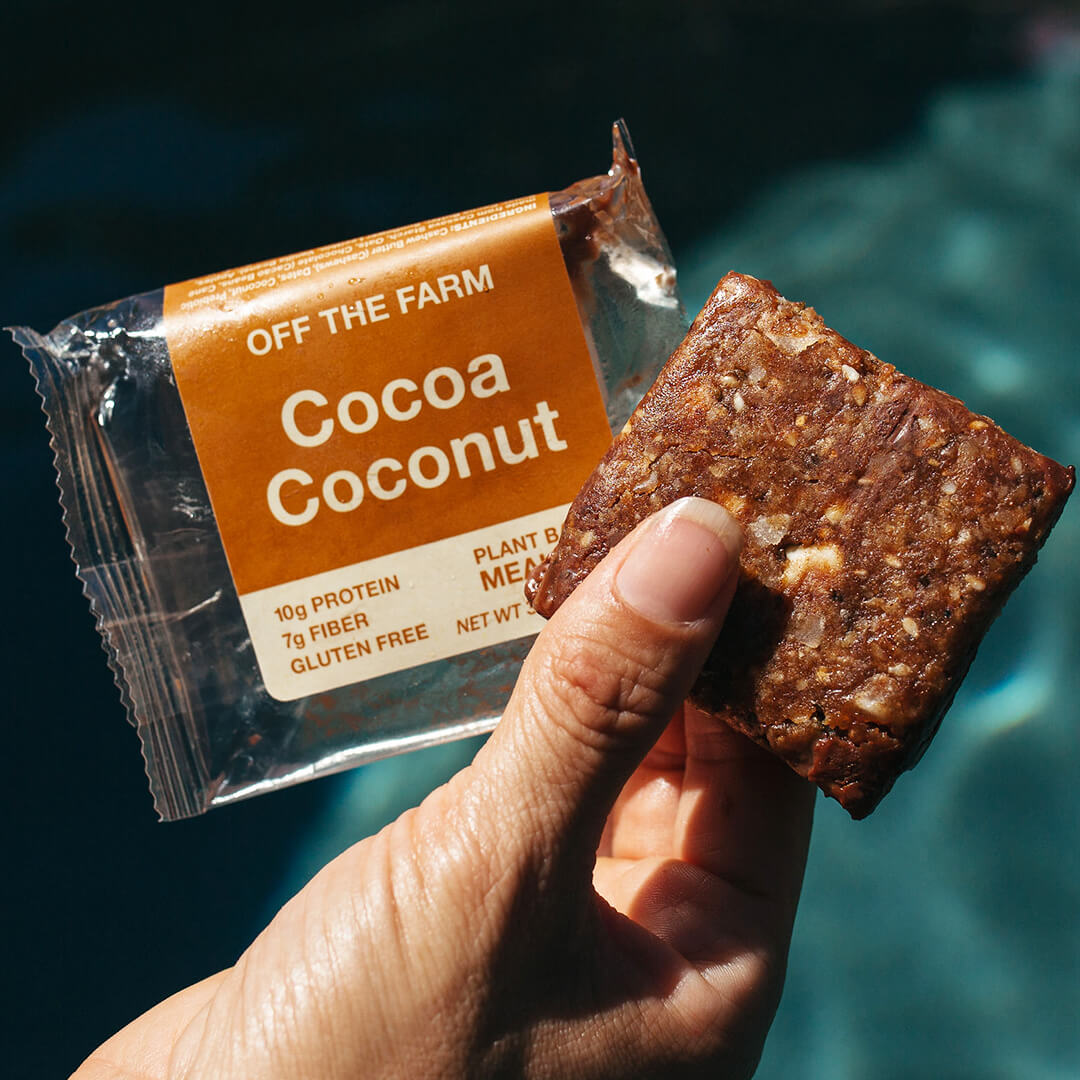 Hand holding a 'Cocoa Coconut' snack bar with packaging against a blurred natural background