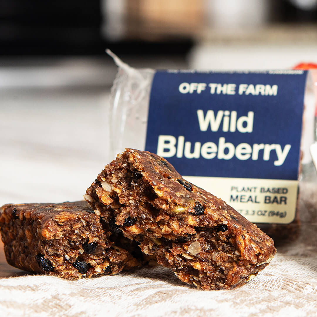 Two wild blueberry meal bars in front of a 'Off the Farm' package on a wooden surface.