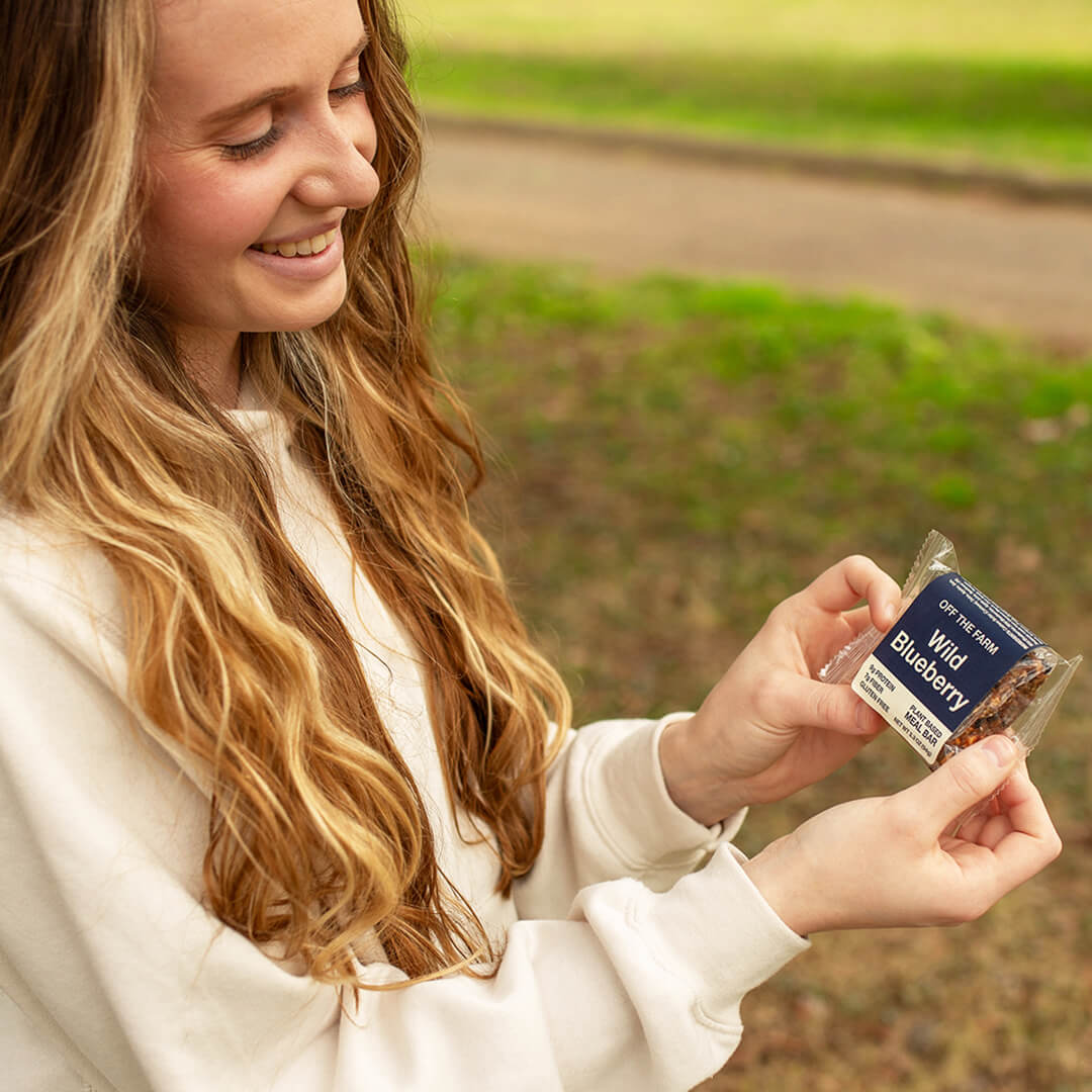 Woman holding an OFF THE FARM Wild Blueberry meal bar outdoors