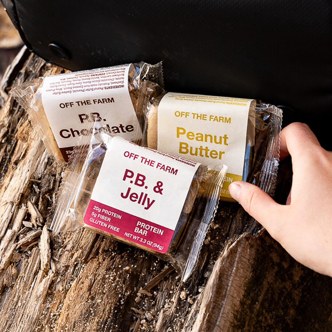 Hand holding a package of 'Off The Farm' protein bars on a wooden surface