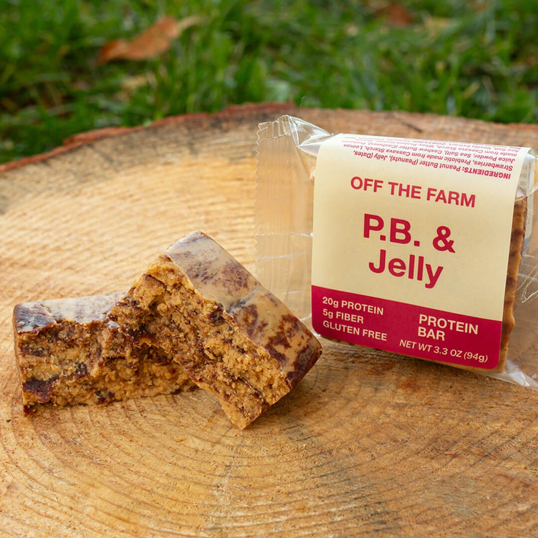 Protein bar with packaging labeled 'Off The Farm P.B. & Jelly' on a wooden surface with grass in the background.